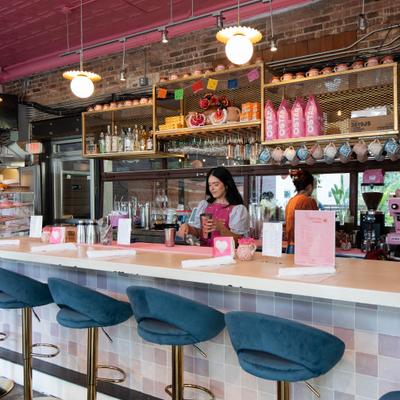 Bartender preparing drinks behind a colorful bar with blue stools and pink decor.