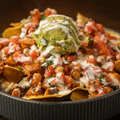 A bowl of loaded nachos topped with chicken, guacamole, tomatoes, and drizzle of sour cream.