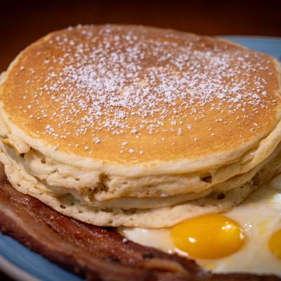 Pancakes served with fried eggs and bacon on plate.