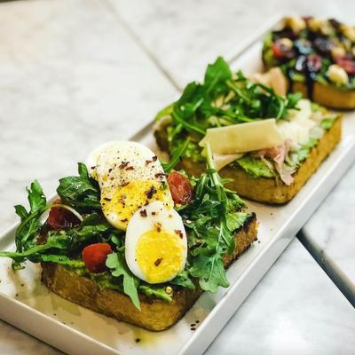 Assorted toasts with various toppings such as arugula, boiled egg, cheese, and prosciutto.