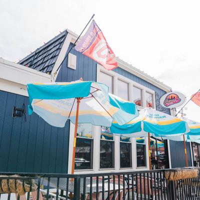 Outdoor view of the restaurant with a blue facade, colorful striped umbrellas, and flags.