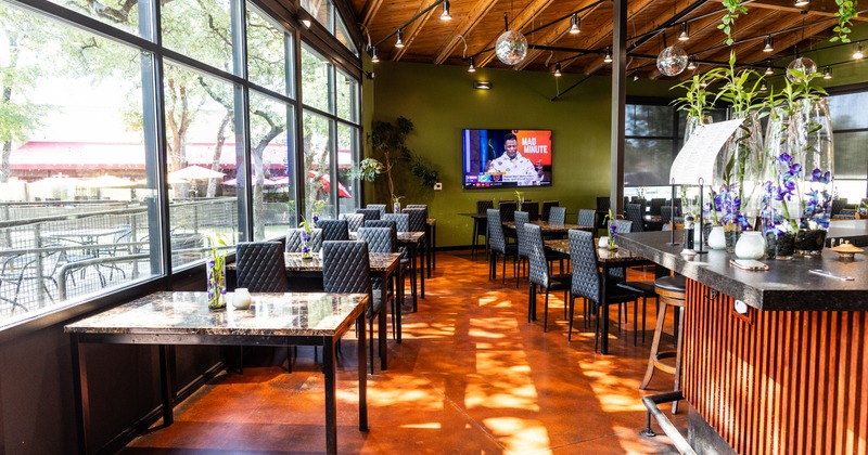 Modern restaurant interior features black quilted chairs, large windows, and a warm-toned floor