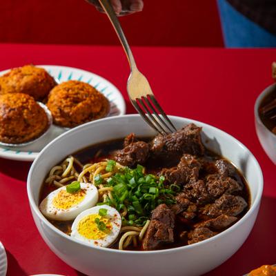 Beef yakamein with fork lifting beef pieces.