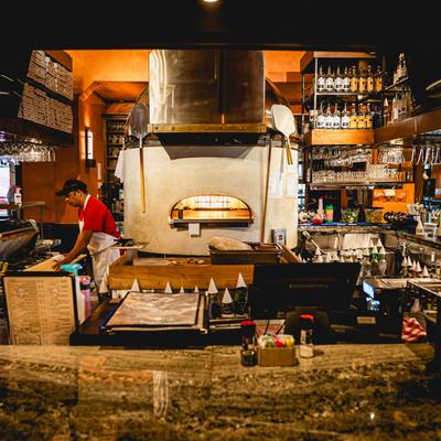 Kitchen with a wood-fired pizza oven, kitchen staff, and a bar.