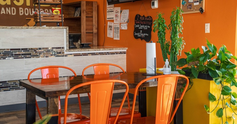 Interior with orange chairs, a wooden table, green plants and a digital menu board.