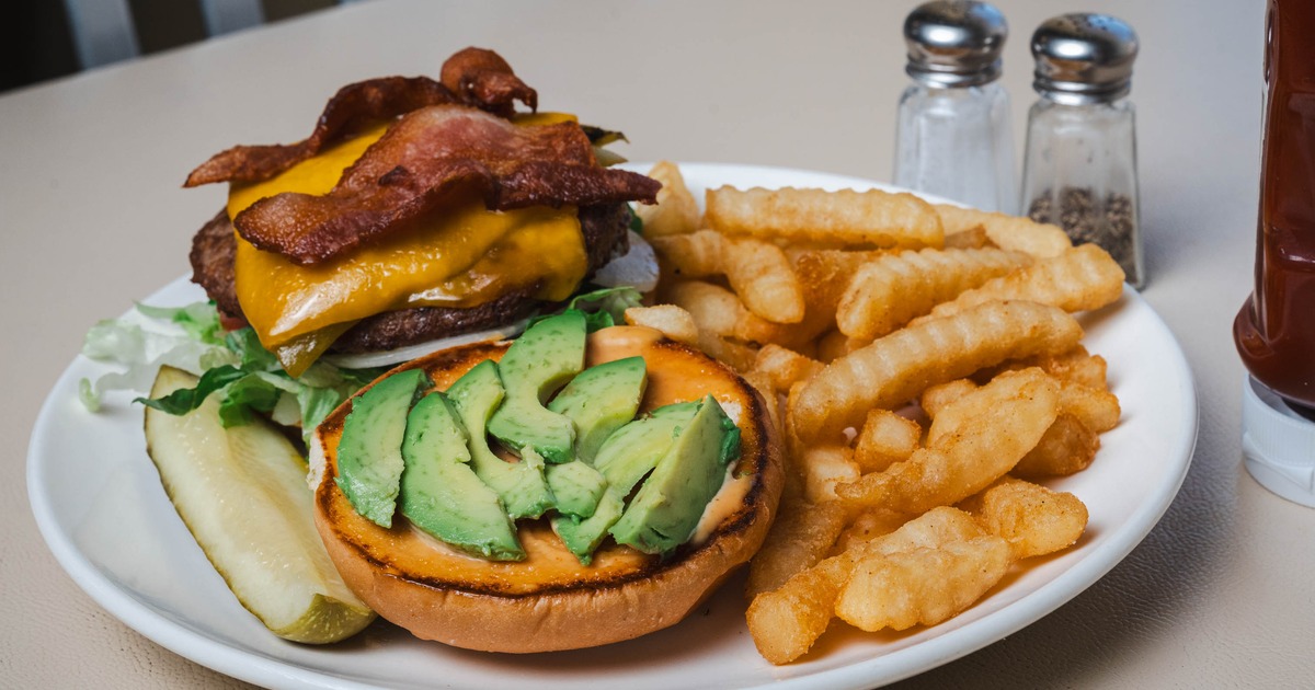 Sunrise Burger topped with bacon and sliced avocado, served with fries and a pickle