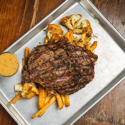 Grilled ribeye steak with fries, fried cauliflower, and sauce.
