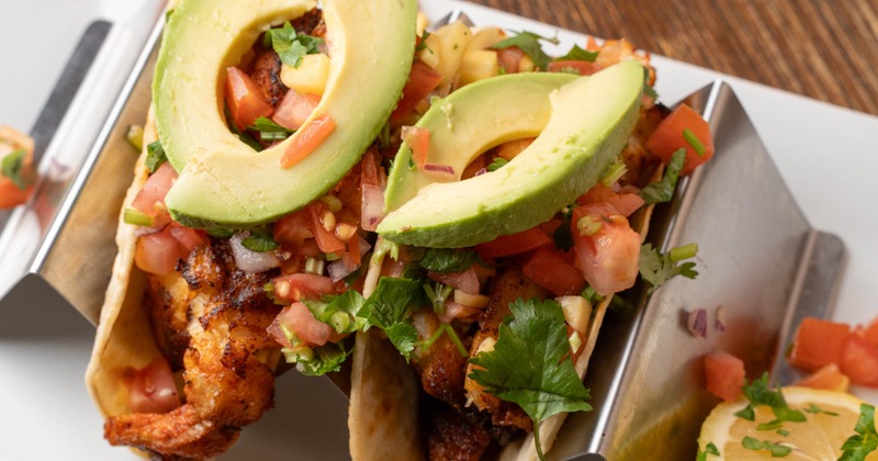 Fish tacos topped with avocado slices and salsa