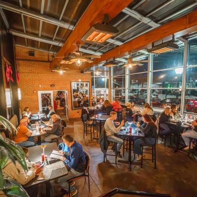 Restaurant dining area with guests at tables near large windows.