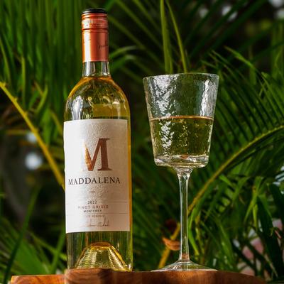 Maddelina wine bottle and glass resting in front of palm branches.