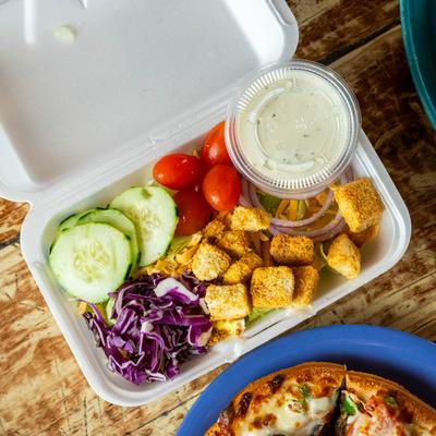 Foam container filled with cucumbers, cherry tomatoes, cabbage, croutons, and ranch.