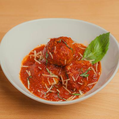 Braised meatballs served in a white bowl, garnished with fresh basil, herbs, and cheese.