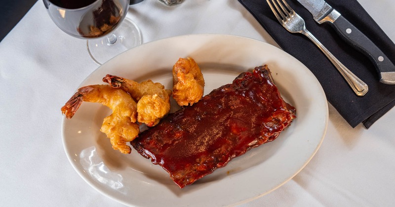 Ribs and Shrimp Combo plate and a glass of red wine on a table