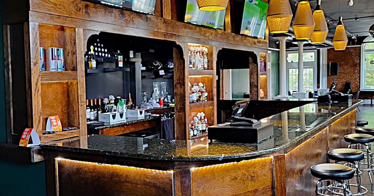 A cozy, modern bar with a dark granite countertop, wooden shelves with bottles