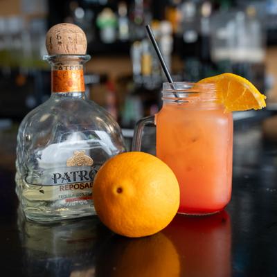 Tequila Sunrise served alongside a bottle of tequila and a fresh orange.