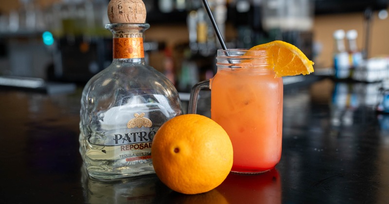 Tequila Sunrise garnished with a slice of orange and served alongside a bottle of tequila
