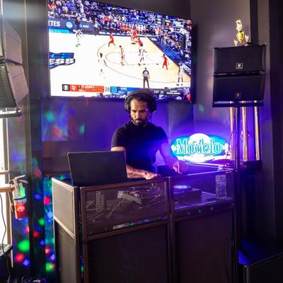 DJ performing on the stage with a large television screen in the background.