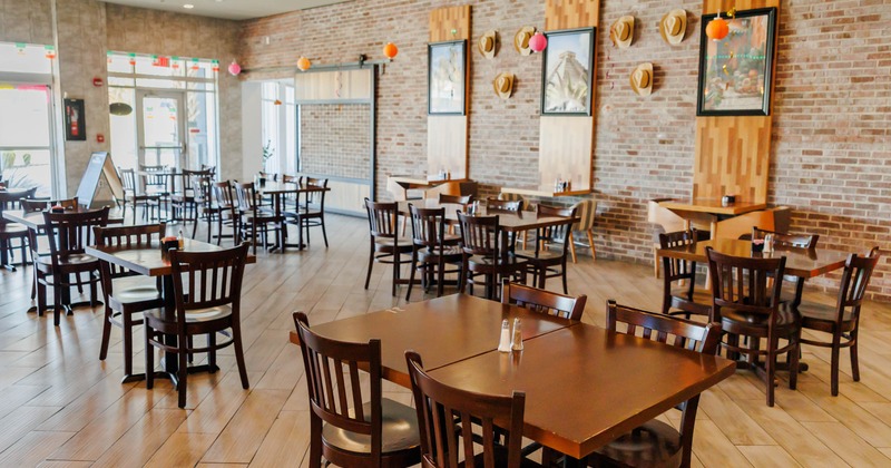 An empty restaurant interior with wooden tables and chairs, brick walls, and decorative elements