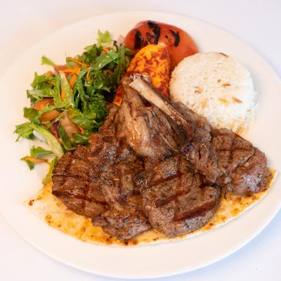 Lamb cops served with rice, a salad, and grilled tomato.