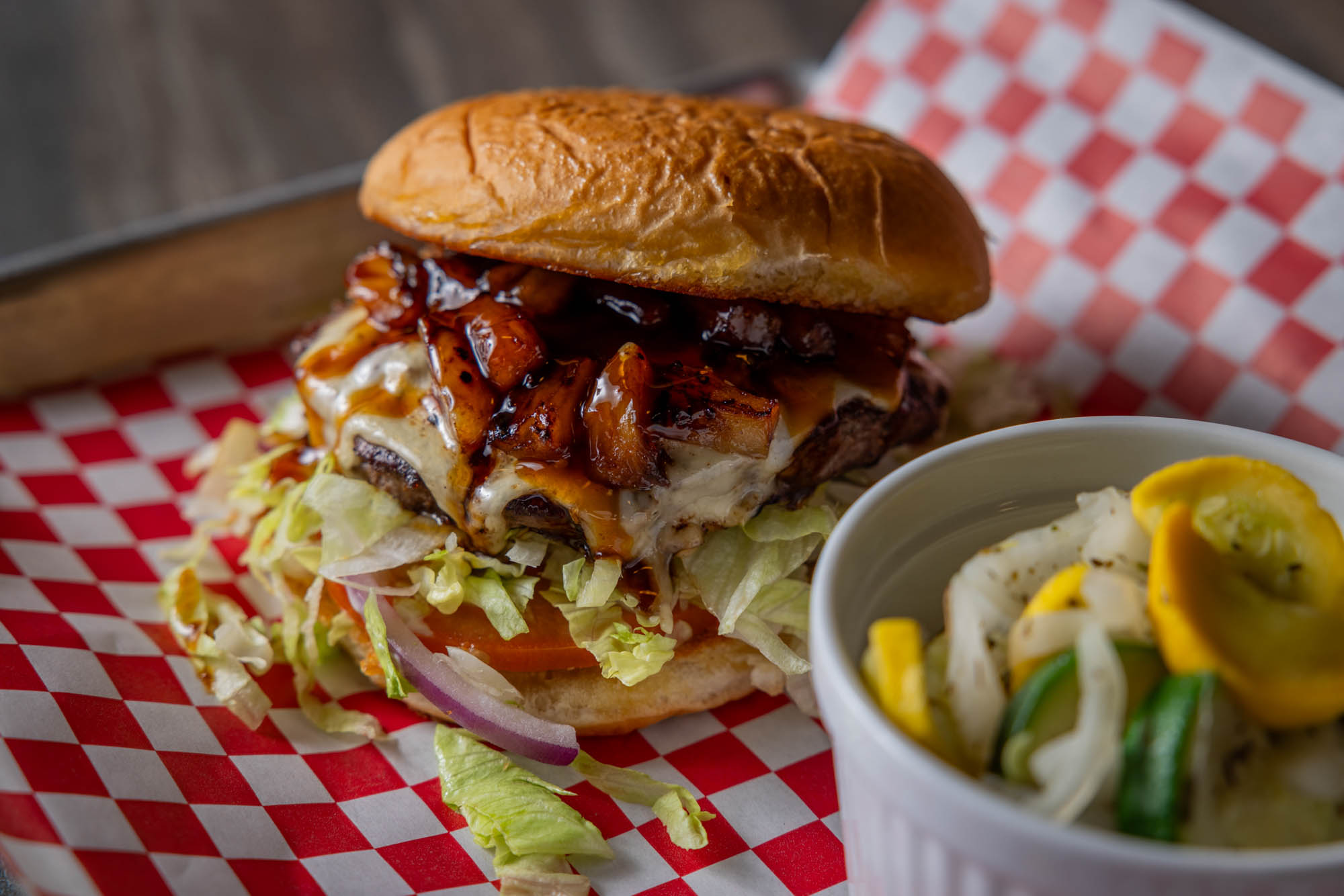Close up of a burger with grilled pineapple and teriyaki sauce. Served with mixed vegetables