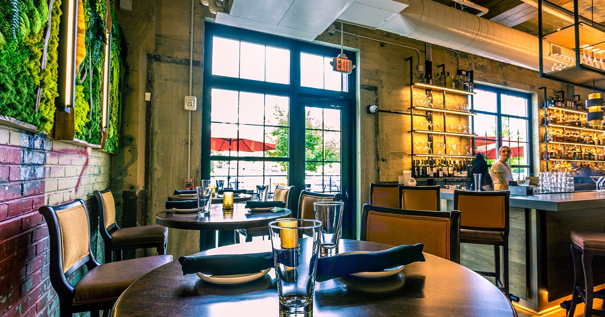 Near the bar, set dining tables by a brick wall decorated with greenery