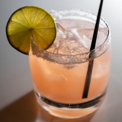 Pink cocktail garnished with a lime wheel and a salted rim.