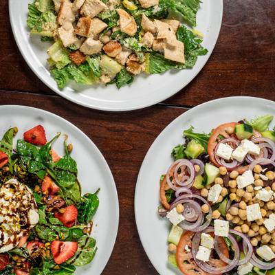 Caesar salad, chickpeas salad, and spinach and burrata salad wit strawberries, overhead view.