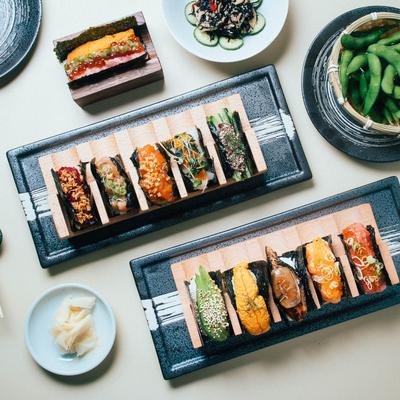 Assorted sushi arranged in wooden trays with edamame, sides, and garnish plates.