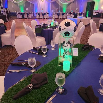 Soccer-themed event hall with blue and green table settings and sports-inspired party decorations.