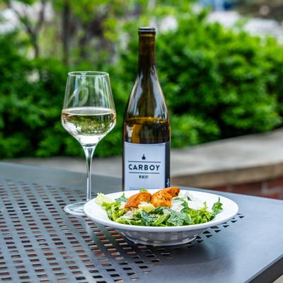 Salad in front of a bottle and a glass of white wine.