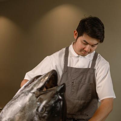 Chef cleaning a large tuna head on a wooden counter.