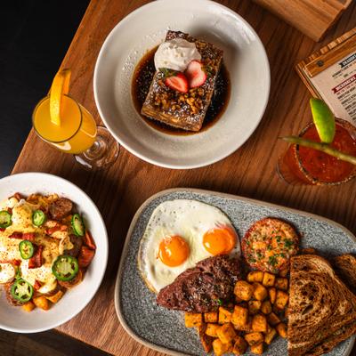 Brunch dishes and drinks served on a wooden table beside a menu.