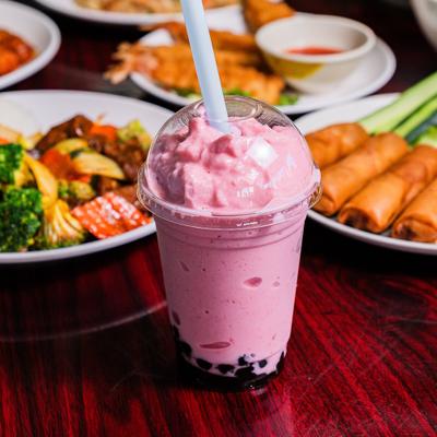 Strawberry boba milk tea with plated dishes in the background.
