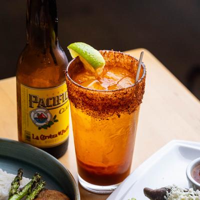 Michelada next to a bottle of beer on a table.