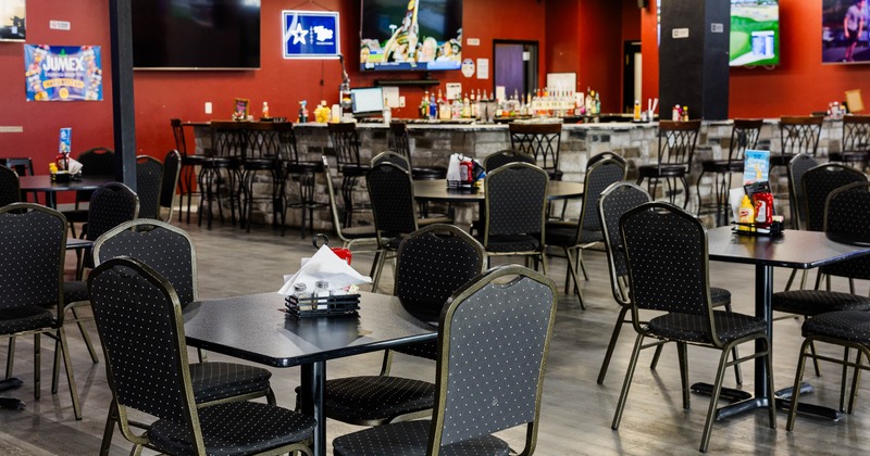 Interior with black tables and chairs, a bar with high chairs and flat-screen TVs on red walls