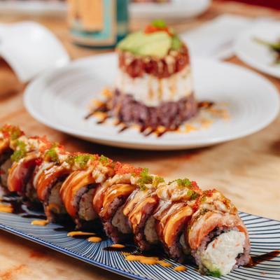 Sushi roll served on a rectangular patterned plate with ahi tower in the background.