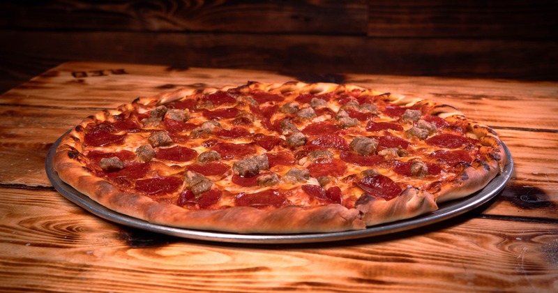 Pepperoni and sausage pizza on a metal pan over a wooden table