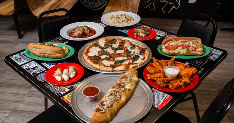 A table filled with pizza, wings, pasta, subs, and cannoli