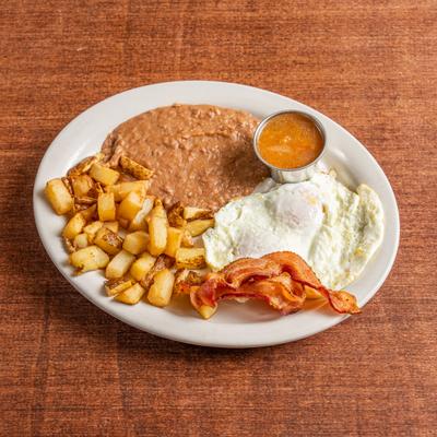 Breakfast plate with fried eggs, bacon, potatoes, refried beans, and sauce.