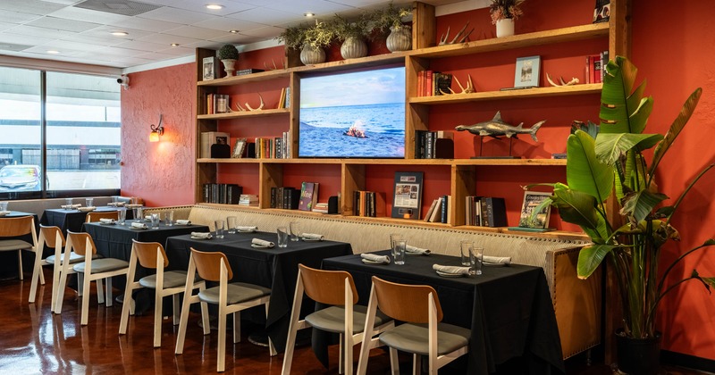 Interior with tables, chairs, and a wooden shelf filled with books and decor items,