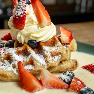 A toasted croissant waffle served on a bed of cream, with fresh berries, and whipped cream.