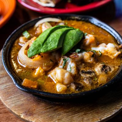 A skillet with shrimp, mushrooms, onions, and avocado slices in an orange broth
