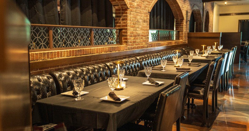 Long dining table with black tablecloth, set with crystal glasses and black napkins, against a backdrop of brick wall