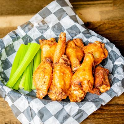Crispy wings and celery sticks in a basket with checkered paper.
