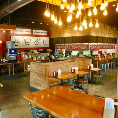 Interior with mix of wooden tables and booths, industrial-style lighting and an open kitchen area.