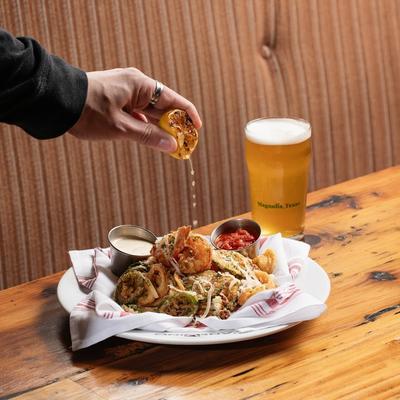 Hand squeezing a charred lemon over a fried seafood plate beside a glass of beer.
