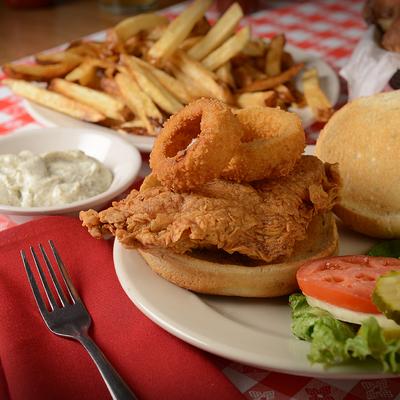 Fried chicken sandwich with onion rings served with a side of fries and dipping sauce.