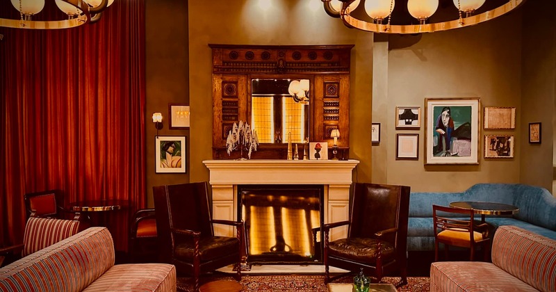 A luxurious living room with a fireplace, ornate mirror, art, plush seating, and velvet curtains