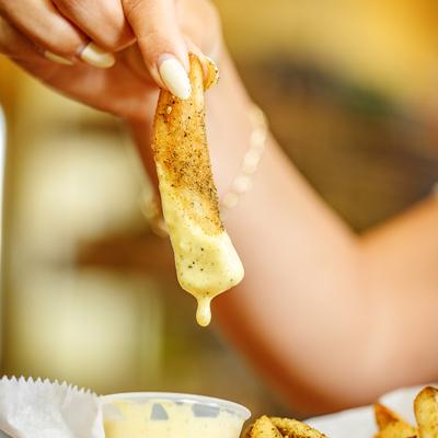 A person holding a dripping fried potato wedge dipped in sauce.