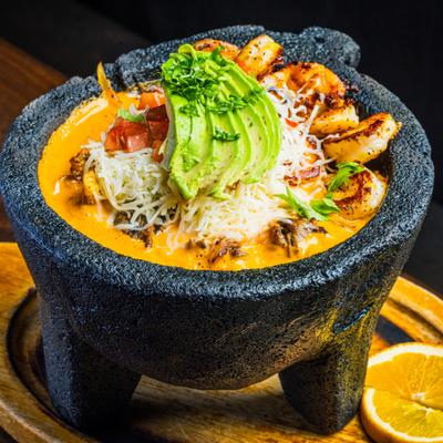 Molcajete bowl filled with shrimp, avocado slices, and melted cheese.